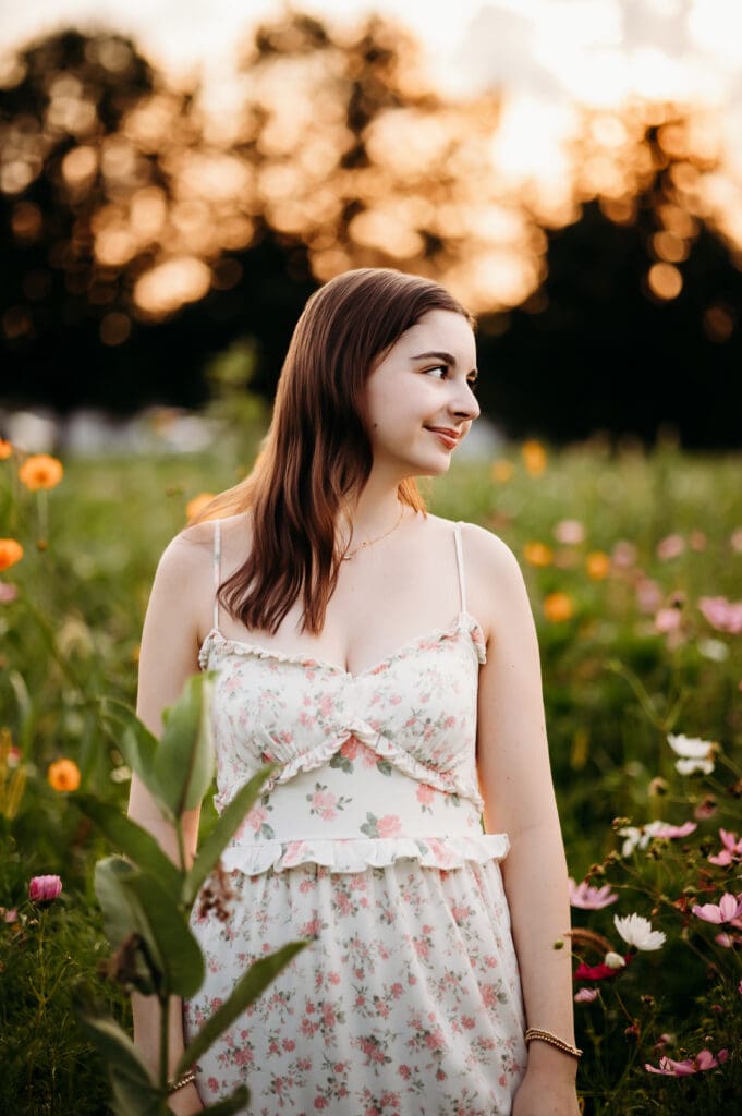 Senior girl standing in wildflower field at sunset, smiling over shoulder – Chicago suburbs senior photographer.