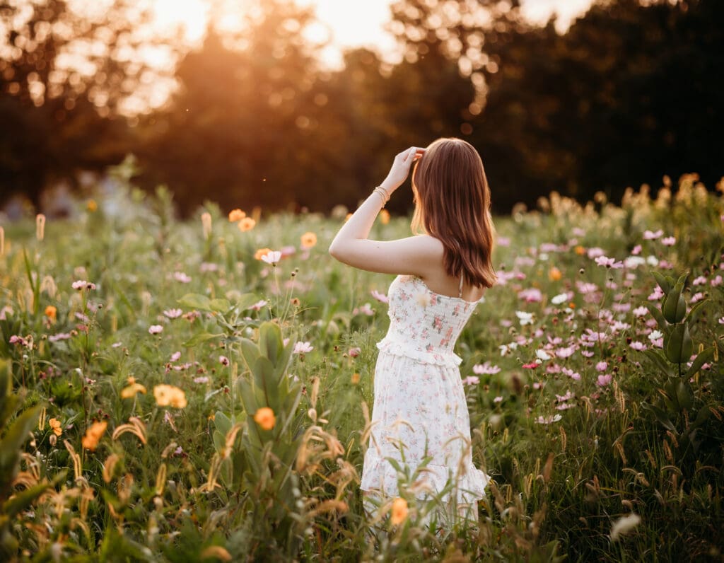 Senior girl standing in wildflower field at sunset, looking over shoulder – Chicago suburbs senior photographer.