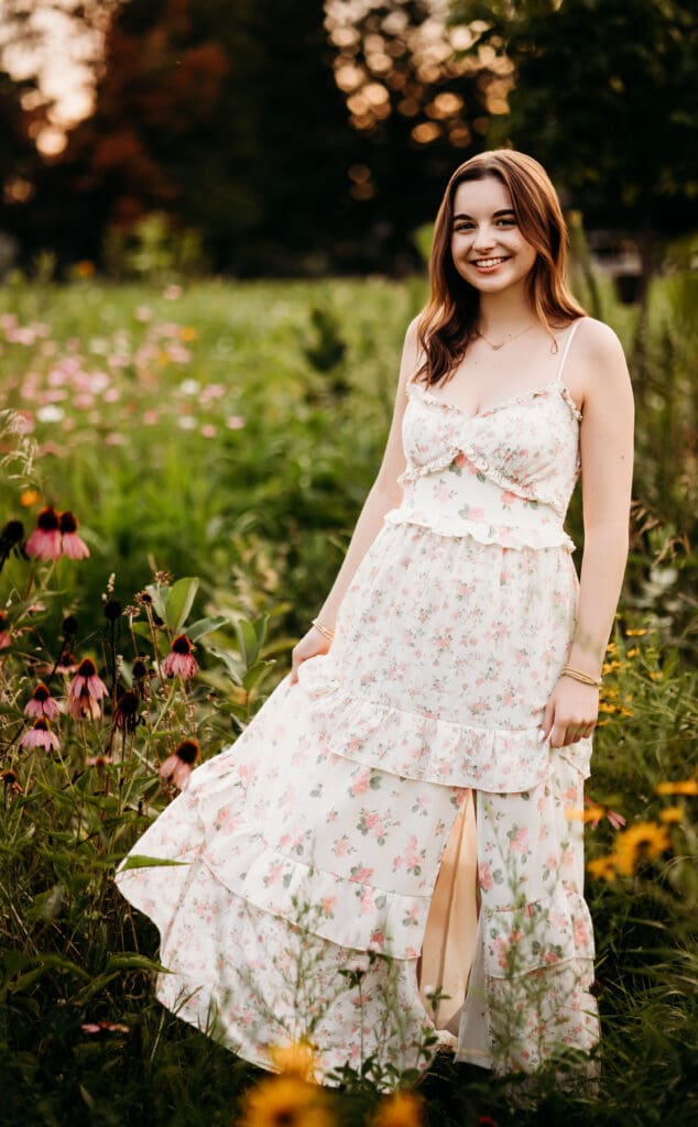 Senior girl standing in wildflower field at sunset, smiling over shoulder – Chicago suburbs senior photographer.