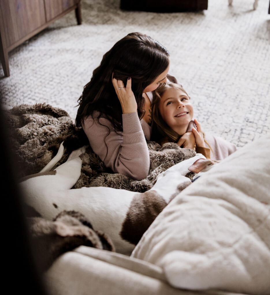 Mother and daughter snuggling on the floor wrapped in blankets during an in-home family session in Oswego IL