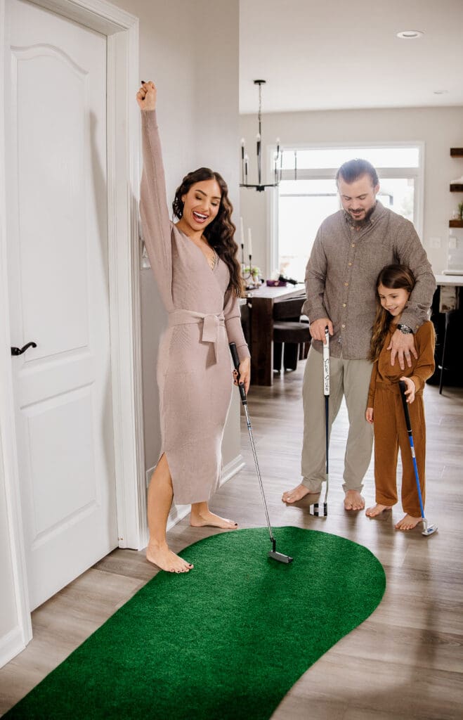 Husband, wife, and daughter laughing together on their hallway putting green during a lifestyle family photography session in Naperville IL