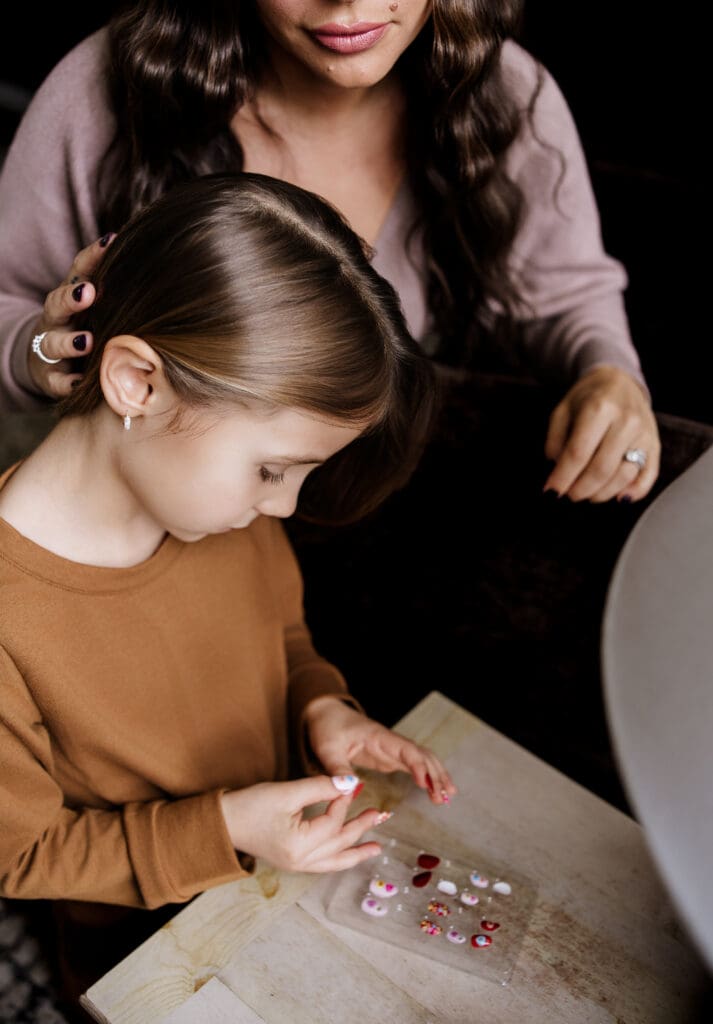 Little girl doing press on nails while her mom watches lovingly, captured by in-home family lifestyle photographer in Chicago suburbs