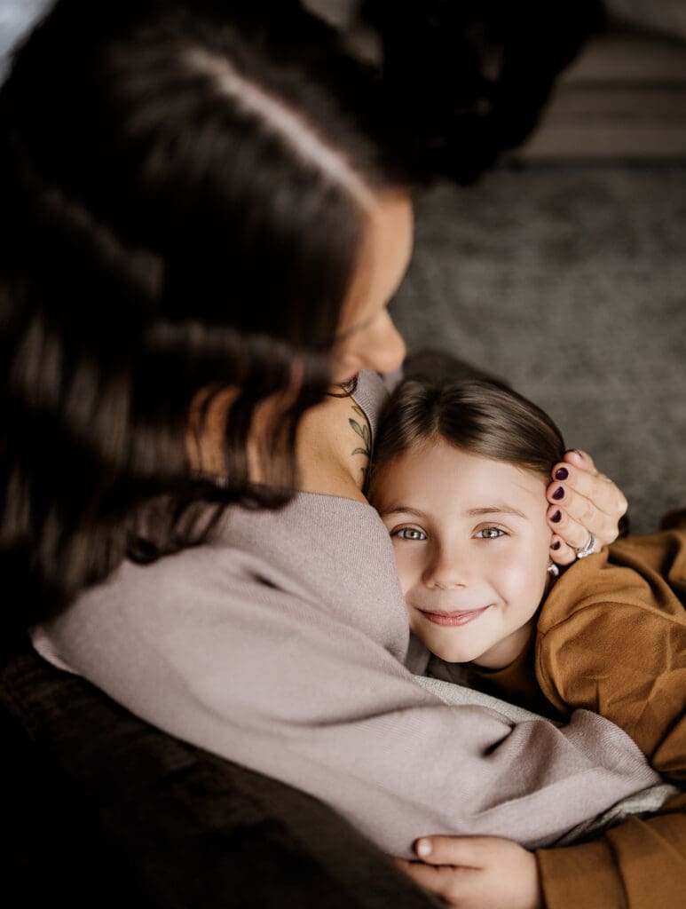 Mom holding her daughter tenderly on the couch during an in-home family lifestyle session in Chicago suburbs